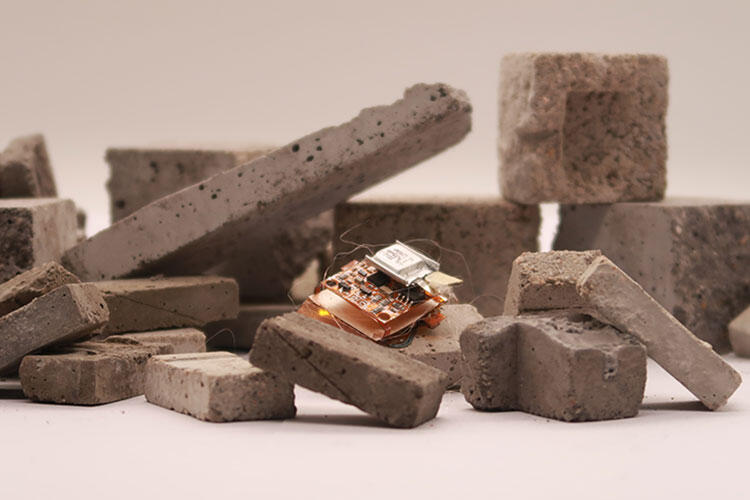 A small metallic robot, about the size of a cockroach, sits on a pile of small bricks.